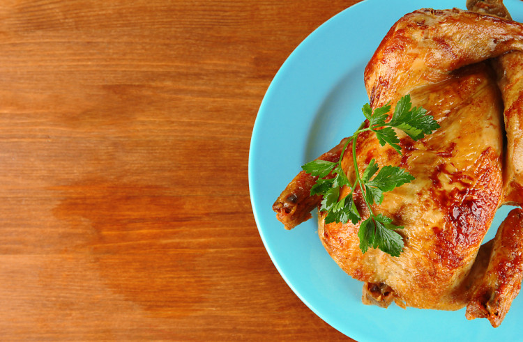 Roasted whole chicken on a blue plate on wooden background