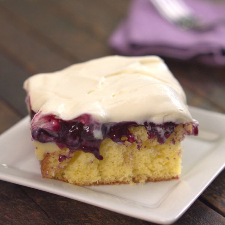 Lemon pudding poke cake topped with blueberry sauce and cream cheese frosting