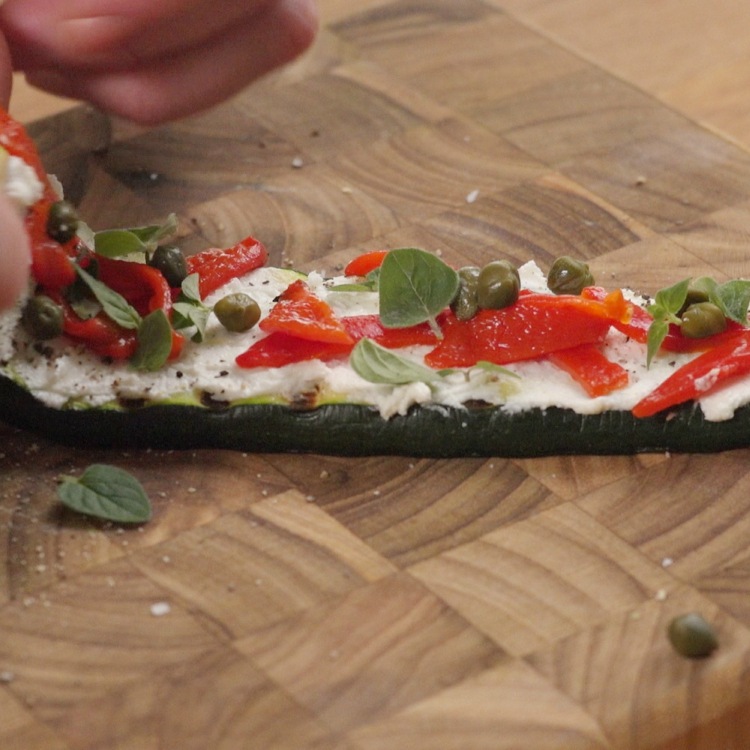 Rolling grilled zucchini slice layered with goat cheese, capers and peppers