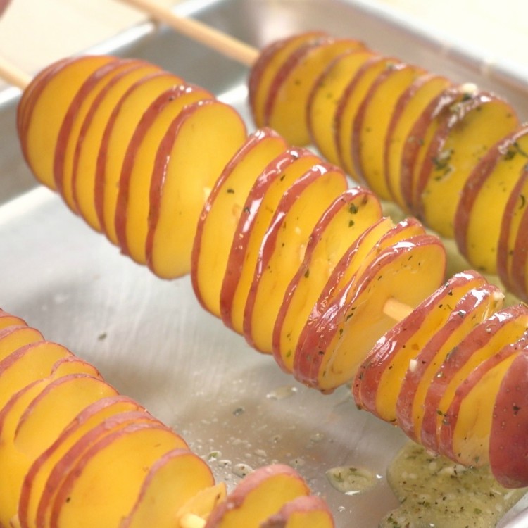 Brushing tornado potato skewer with melted garlic herb butter