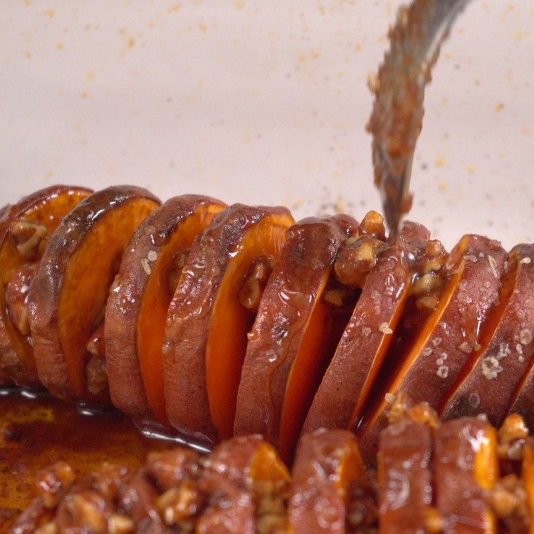 Drizzling hasselback-cut sweet potatoes with maple pecan mixture